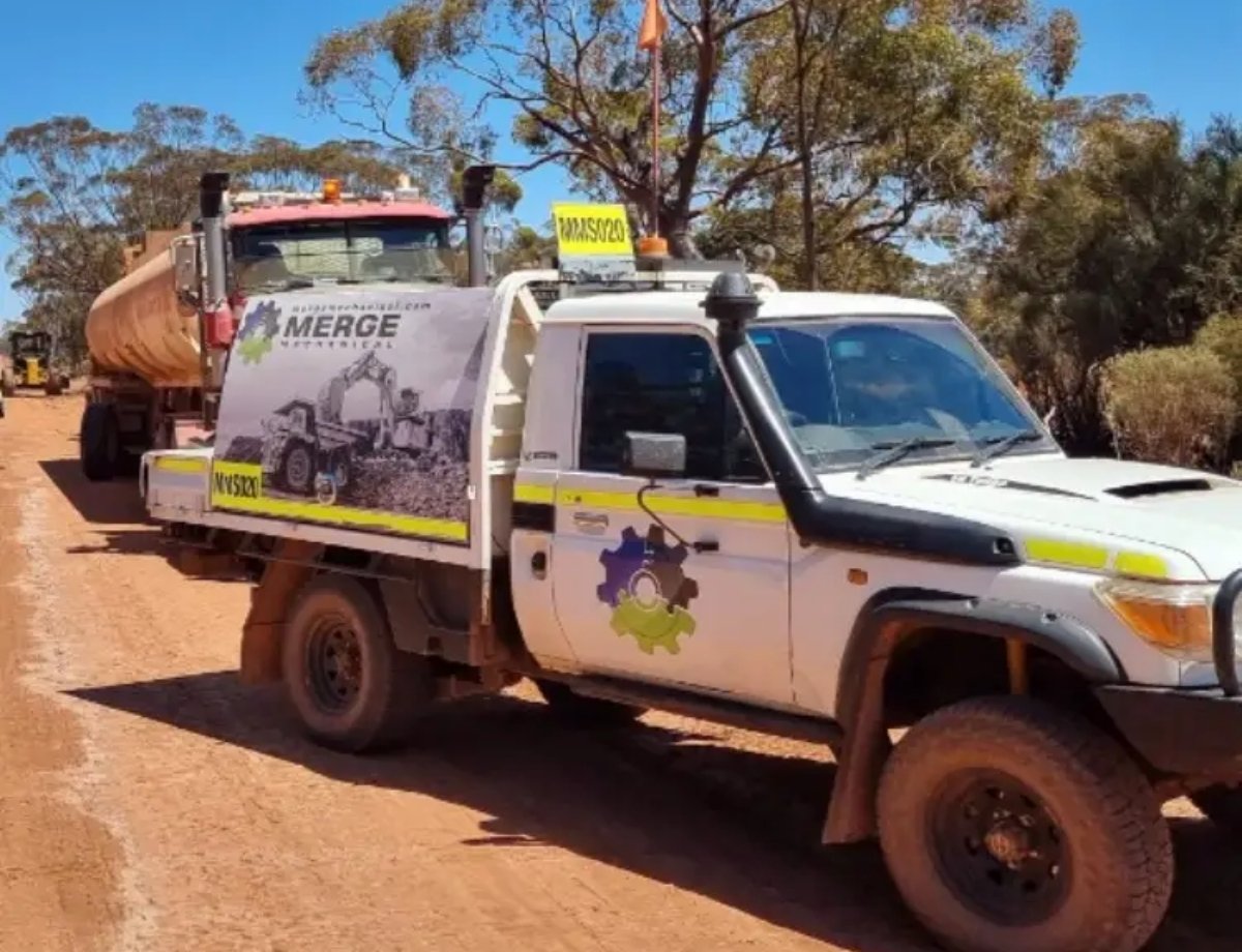Service truck from Merge Mechanical driving on a dirt road alongside a large water tanker truck, ready for heavy equipment maintenance projects.