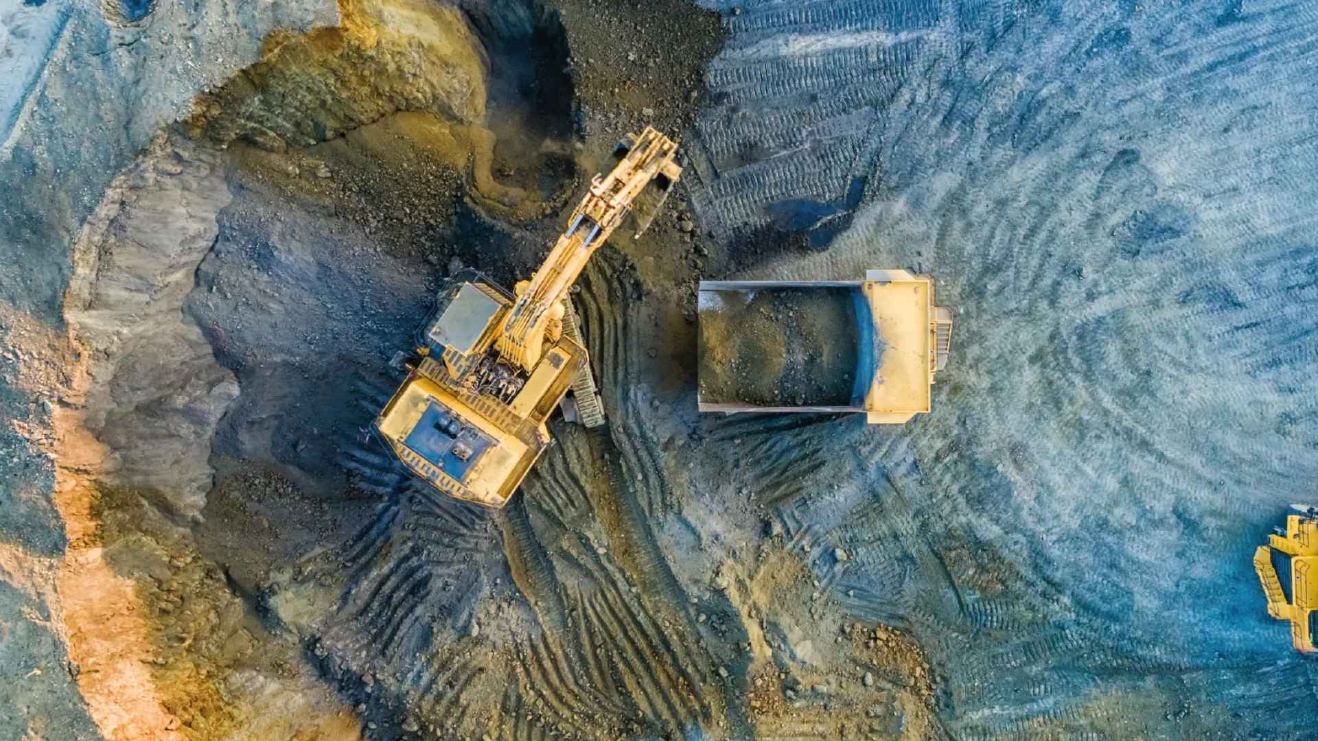 Aerial view of heavy machinery and dump truck at a mining site, emphasising the scale and need for industrial equipment maintenance.